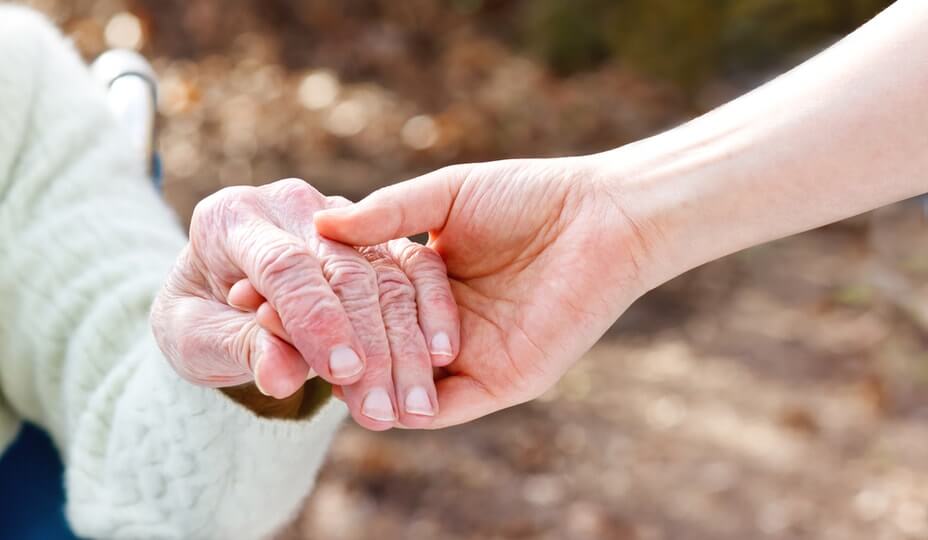 Préposée tenant la main d'une vielle dame dans son fauteuil roulant à l'extérieur d'une résidence pour personnes âgées