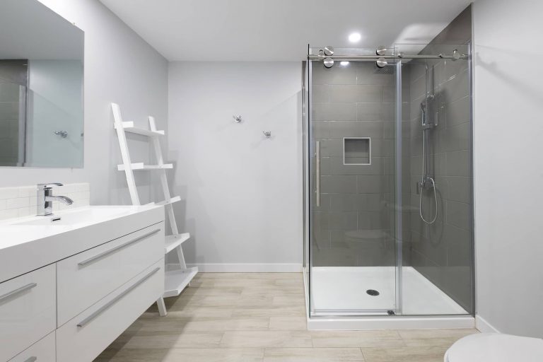 Salle de bain rénovée dans un sous-sol avec douche en céramique et vanité blanche