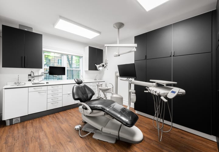 Salle de traitement dans une clinique dentaire, rénovée avec plancher en bois, murs blancs et des armoires noires.