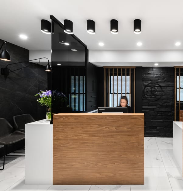 A contemporary style dental reception area, with white marble floors and black walls, and a wooden reception desk at the center