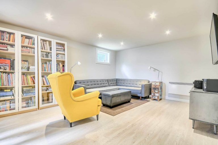décoration de sous-sol avec bibliothèque, chaise jaune et divan en L gris
