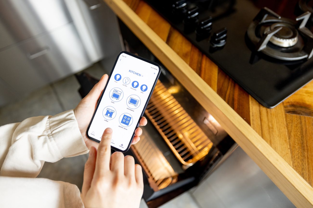 Woman holding phone with smart home app, controlling kitchen appliances remotely