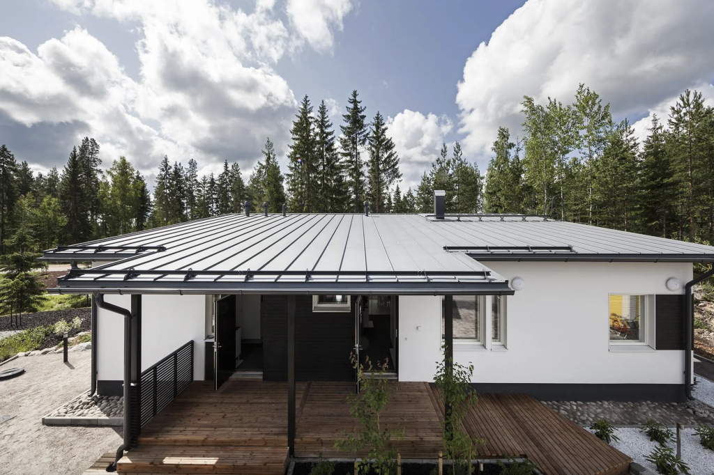 Flat black metal roof on a white bungalow near a pine forest