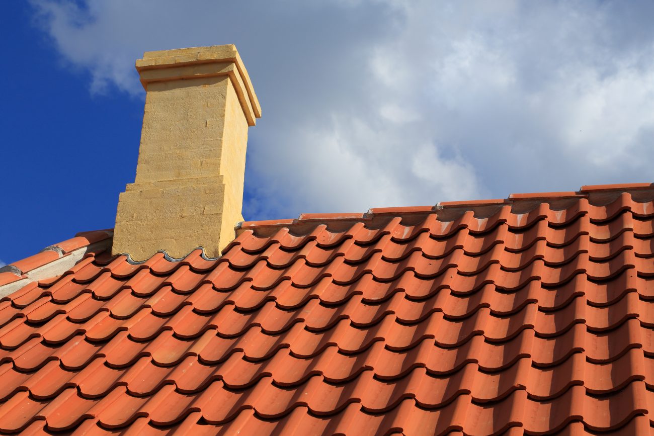 Toiture en tuiles d’argile orangée sur un toit en pente avec cheminée jaune