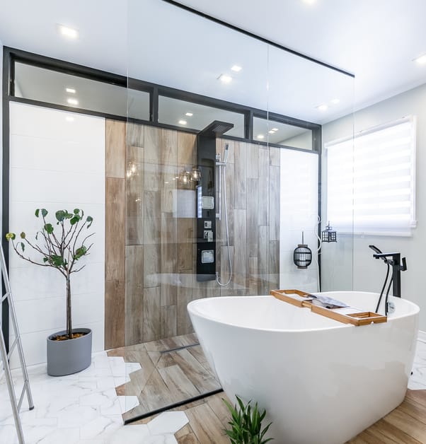 Behind a large glass panel is a walk-in shower with sections of white and wood tiles.