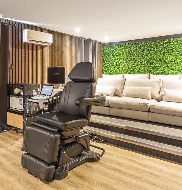 This zen projection room features a green wall, large comfortable sofas for guests, and an ultrasound chair for the pregnant parent