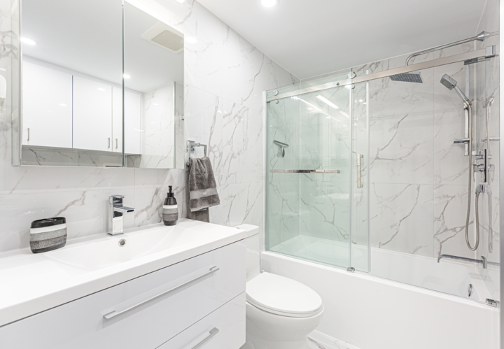 A modern bathroom featuring white marble floors and walls, a white vanity, and a white tub shower.