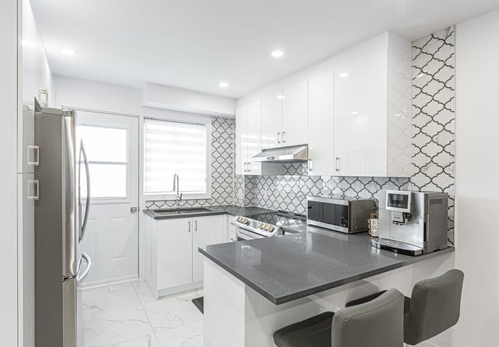 Bright contemporary kitchen with white cabinets, grey countertops, and tile backsplash