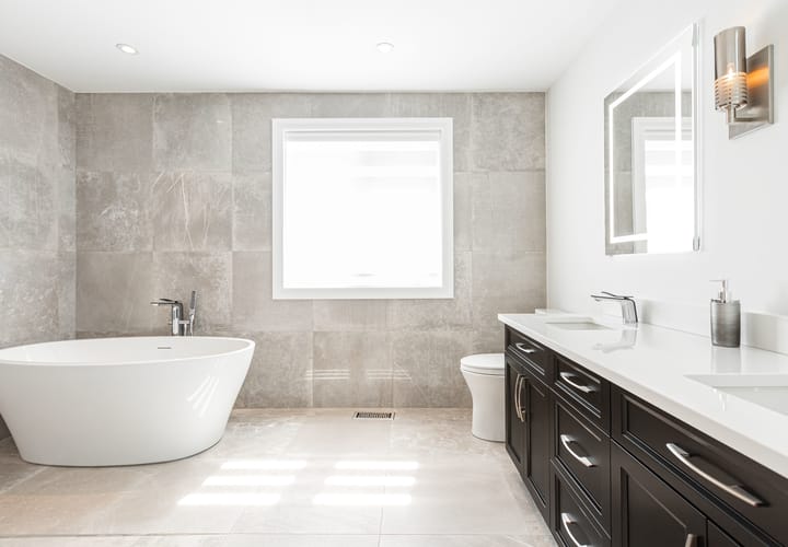 A neutral bathroom with a freestanding tub, a toilet, and a dark double vanity