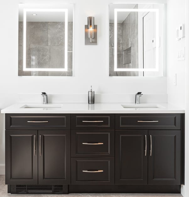 A beautiful dark double vanity with silver handles, silver faucets, and light-up mirrors