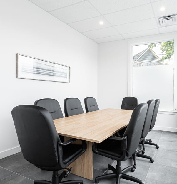 A conference room with several black office chairs surrounding a large wooden table.