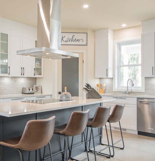A fully equipped white and grey kitchen, with a large island with brown leather bar stools