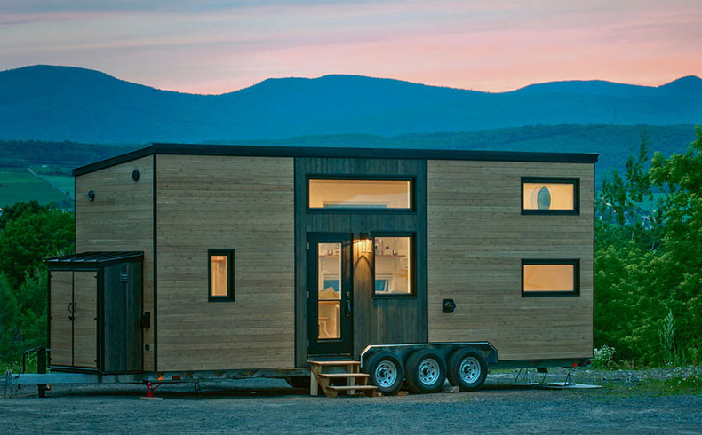 wooden tiny home on wheels with mountains in background 