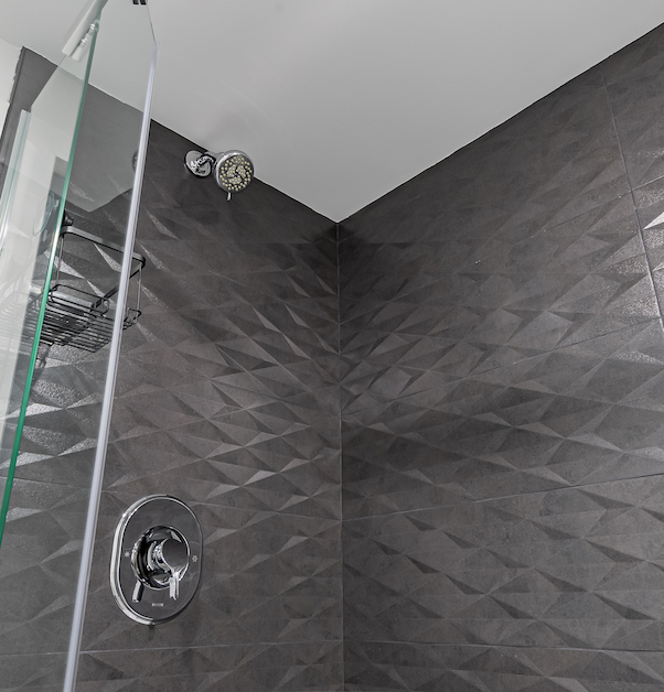 black walk-in shower with glass door, shower head and textured tiles