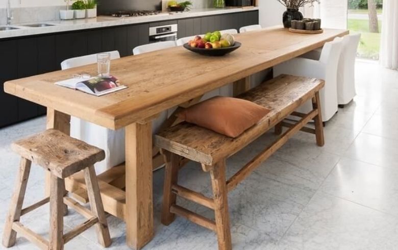 grande table en bois lourd servant d'îlot de cuisine avec des bancs en bois du même matériau
