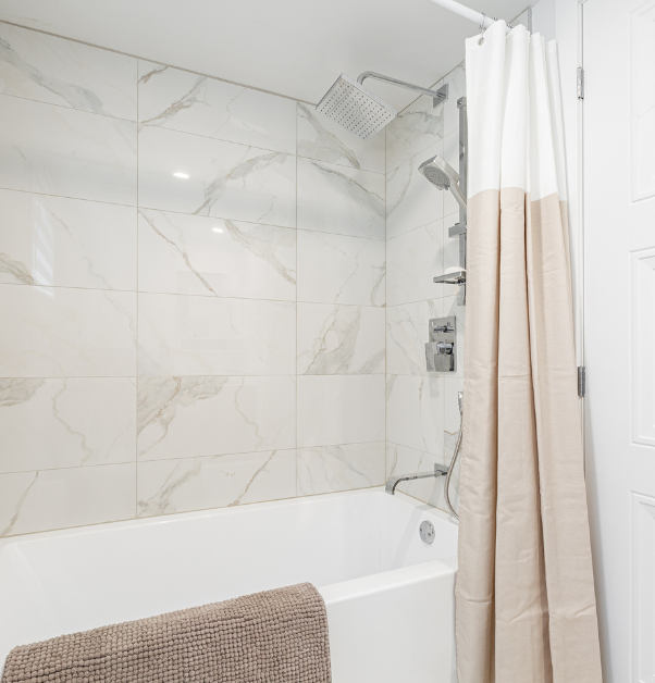 Tub shower with taupe marble tiles in basement bathroom