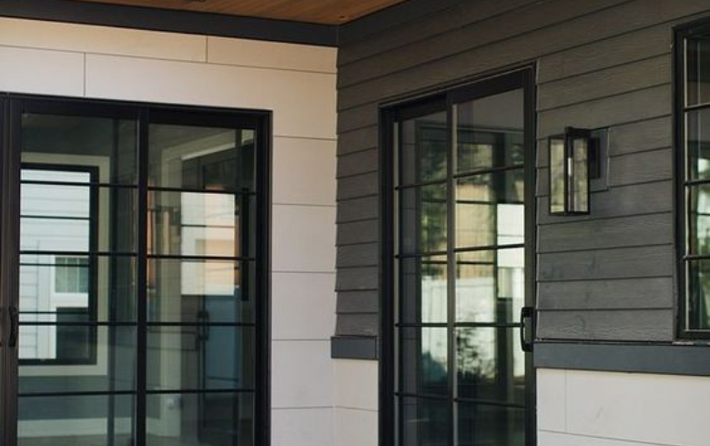 Entrance of a house with white and grey wood fiber siding and black glass doors