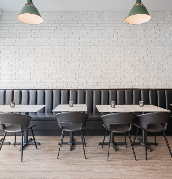 Restaurant dining room with banquette, black chairs, and white brick wall