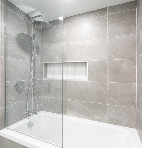 Baignoire-douche rénovée avec robinetterie argent, murs de céramique gris veiné et panneau de verre dans un projet de rénovation multiple