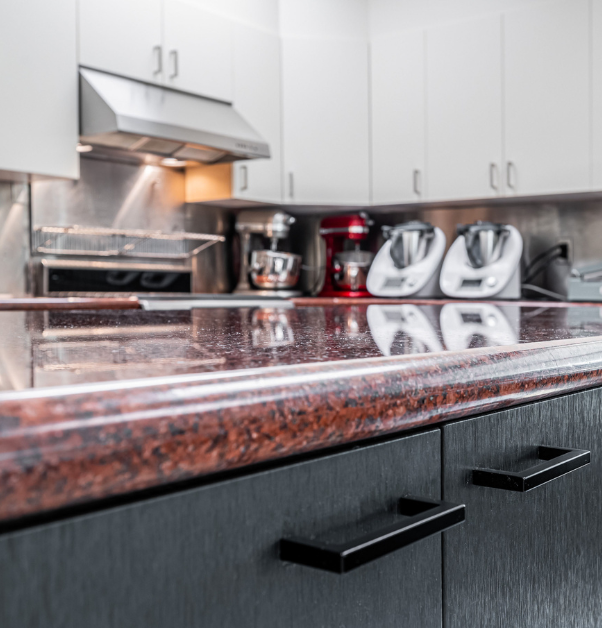 Vue rapprochée du comptoir de préparation en granite brun avec portes en polymère noir mat au centre d'une cuisine industrielle rénovée