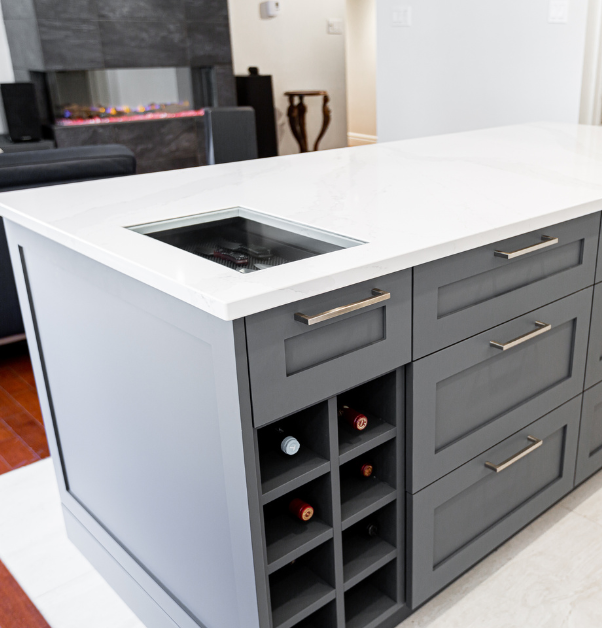 Central kitchen island with glass insert in white quartz countertop, built-in wine storage, and dark grey cabinets