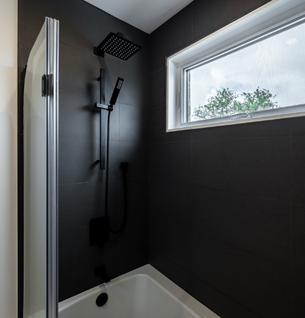 Renovated tub shower with black faucets and walls with black rectangular ceramic tiles