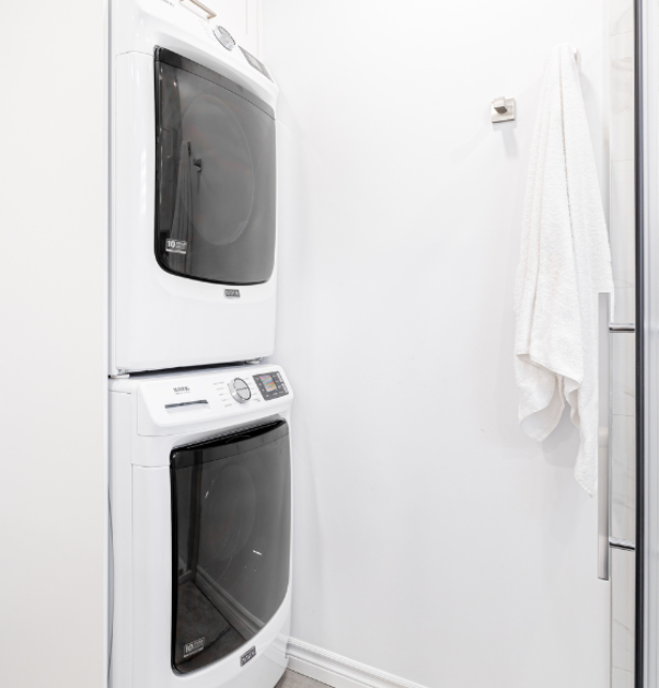 Modern white washer and dryer stacked vertically in a new white bathroom