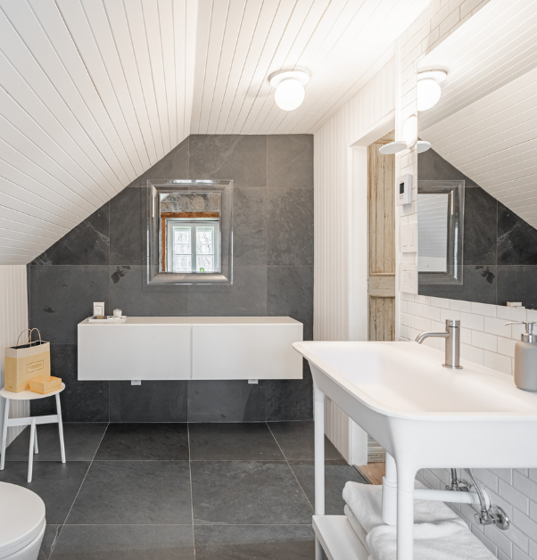 Salle de bain rénovée avec plancher et mur en grandes tuiles d'ardoise, maquilleuse flottante et évier blanc sur pattes