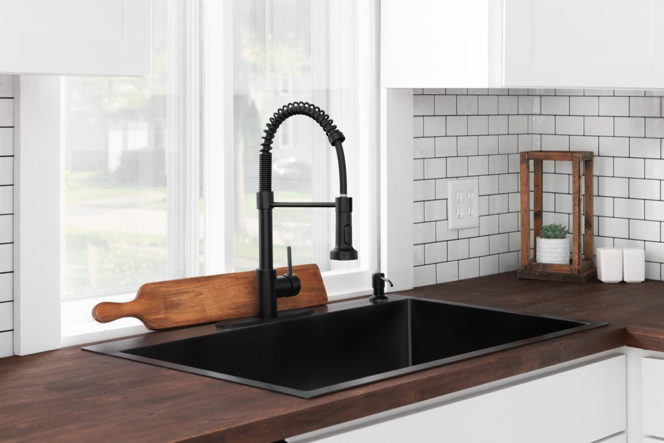 Black sink and faucet in a white kitchen with dark brown countertop