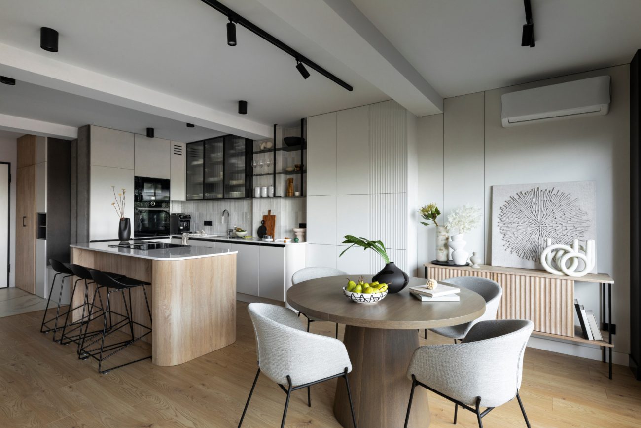 Modern composition of a kitchen area with rounded island, black counter stools, open shelves and large window