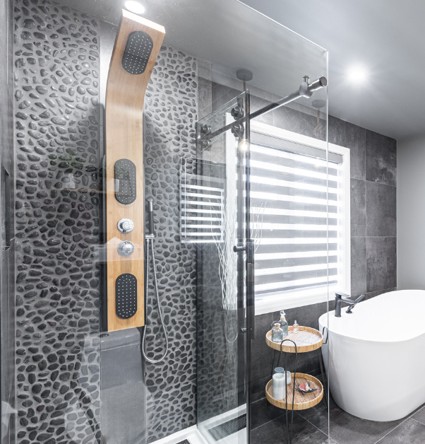Salle de bain rénovée inspirante avec douche à l'italienne avec colonne de douche effet bois clair, parois de verre, dosseret de galets et bain autoportant, transformation inspirante