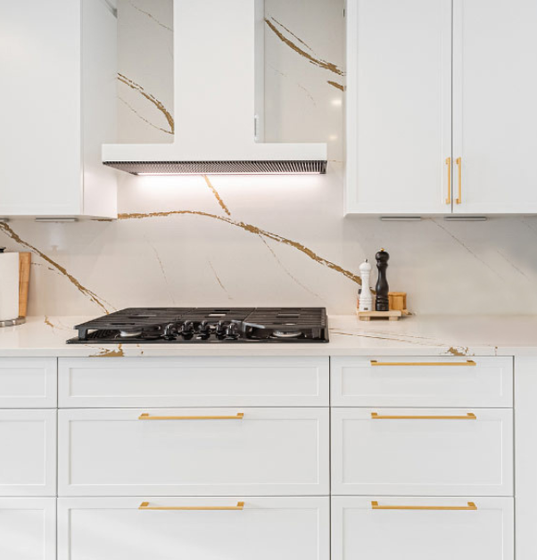armoires de cuisine blanches avec poignées dorées, cuisinière et dosseret en marbre veiné