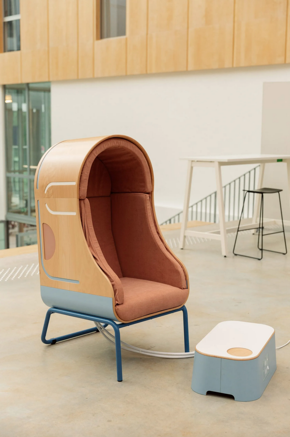 Wooden shell armchair with inflatable cushions inside, and footrest, set in a large office space