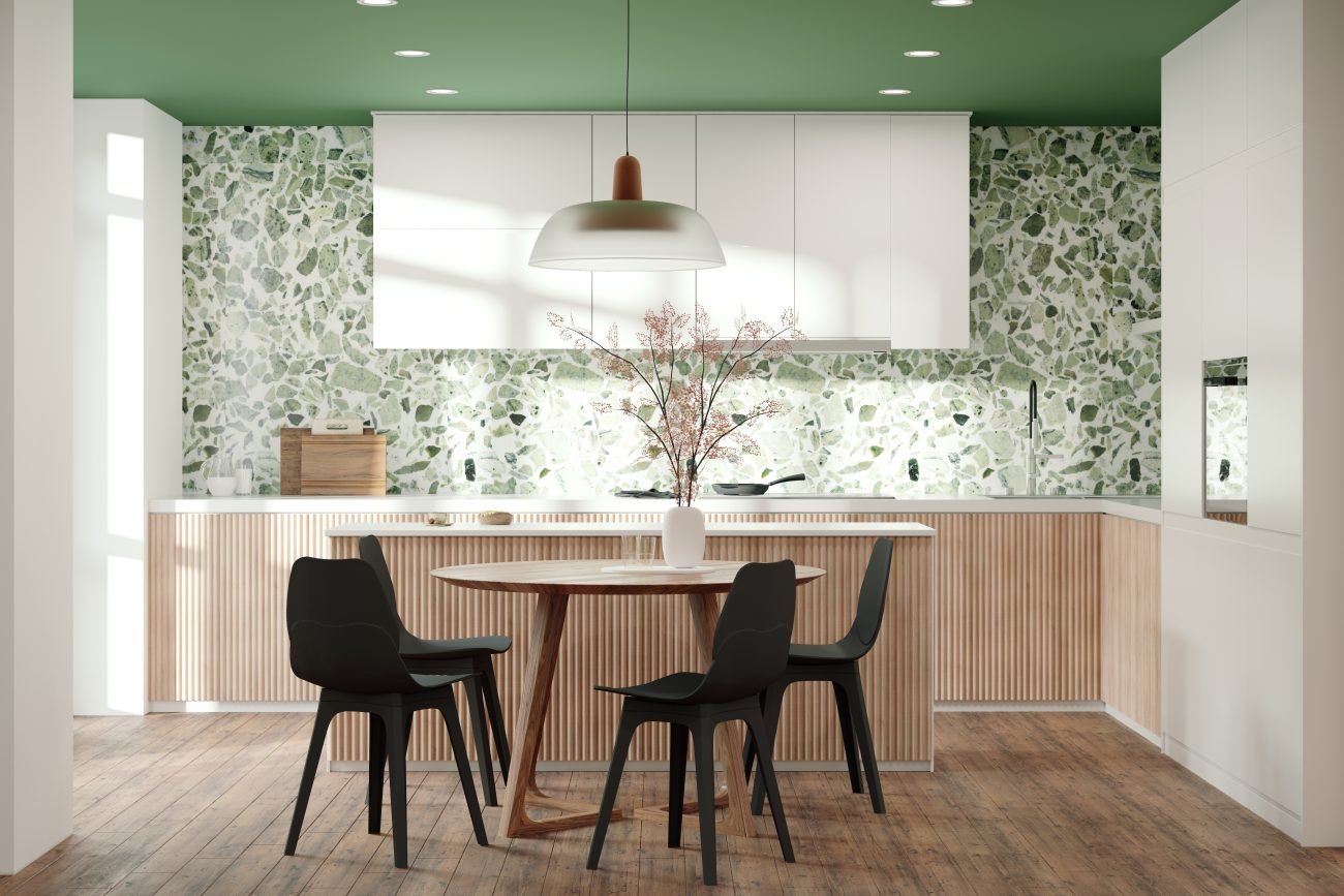 Cuisine avec mur en terrazzo vert, rangements muraux blancs, armoires et îlot décoré de panneaux en bois cannelé, table en bois et chaises à coque noire