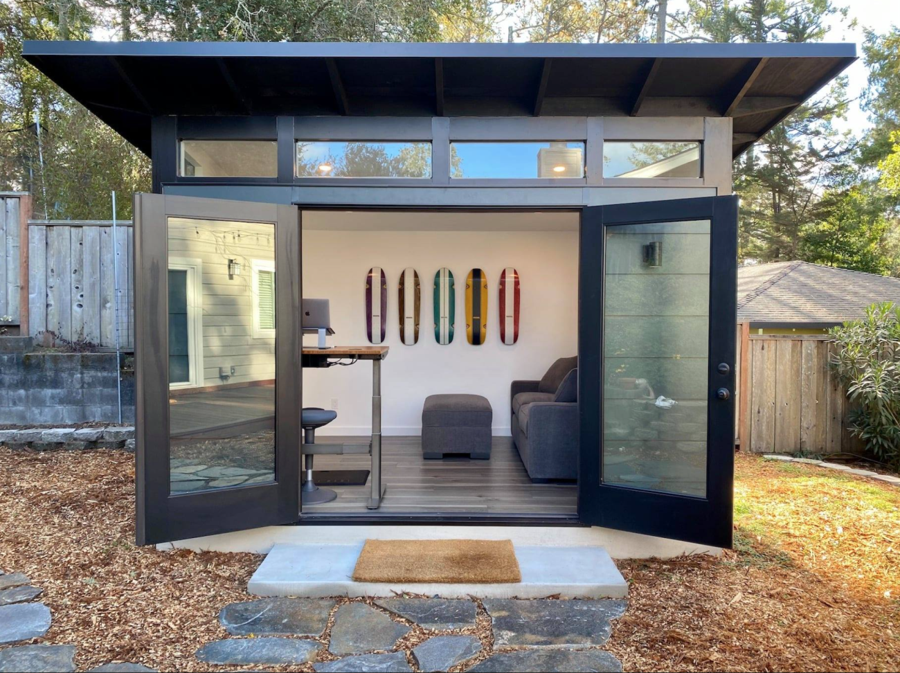 Home office set up in a garden studio with double glass door, workbench-style table, sofa and ottoman, skateboards hanging on the wall