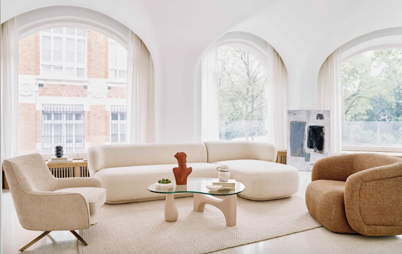 Salon à fenêtres en arches, canapé modulaire blanc crème, fauteuils aux formes arrondis et table basse de forme organique