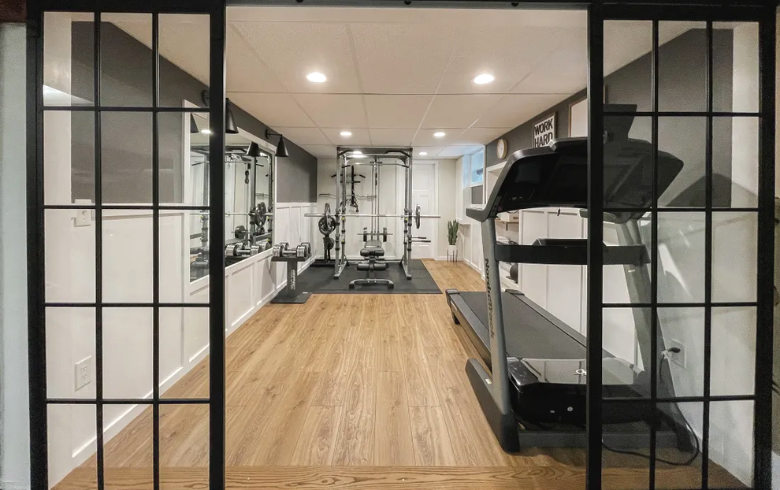 salle de gym au sous-sol avec machines d'entraînement et portes en verre quadrillées