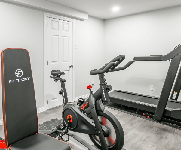 Beautiful home gym featuring bright walls, grey flooring, stationary bike, bench press, and treadmill