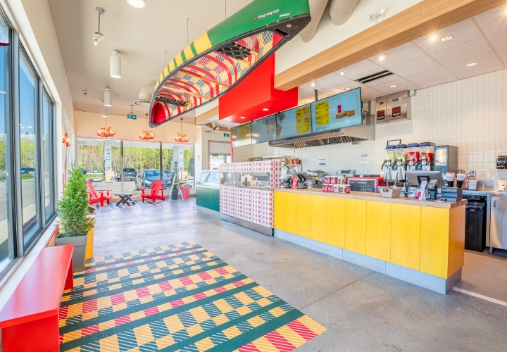 Traditional BeaverTails restaurant featuring bright colours, large windows, digital menu boards, concrete floors, and a canoe suspended from the ceiling.