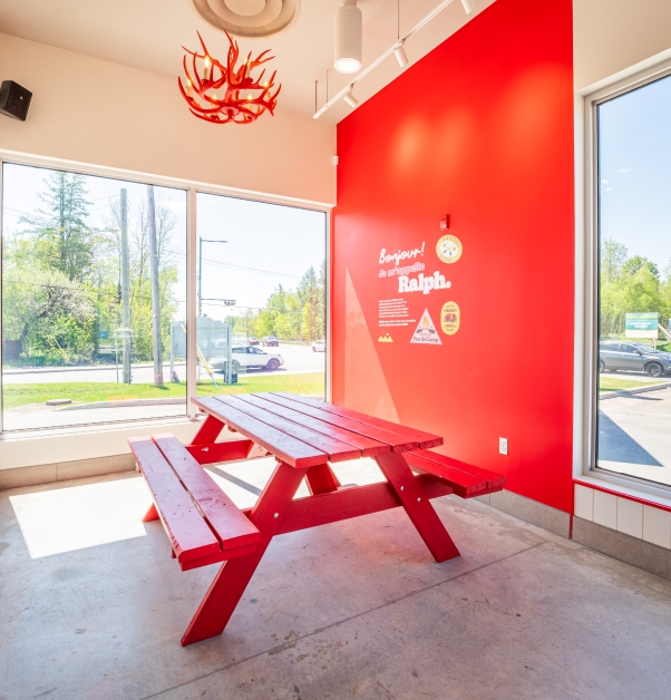 A bright red picnic table with hanging red pendant light beside large windows and a red wall inside a BeaverTails restaurant.