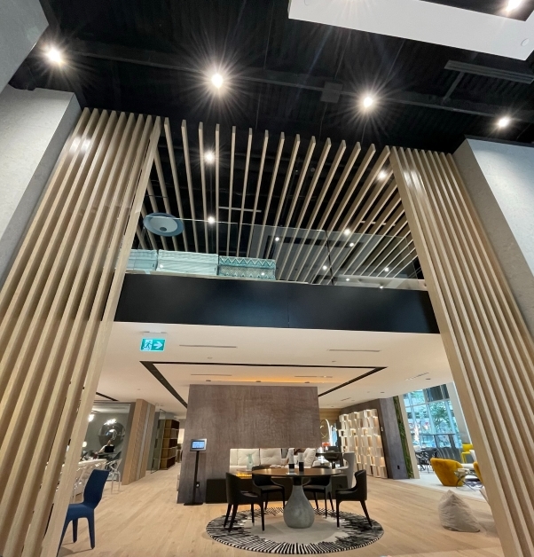 Grands claustras du plancher au plafond en bois teinte naturelle dans un magasin de meubles haut de gamme, mezzanine avec garde-corps en verre, plafond noir.