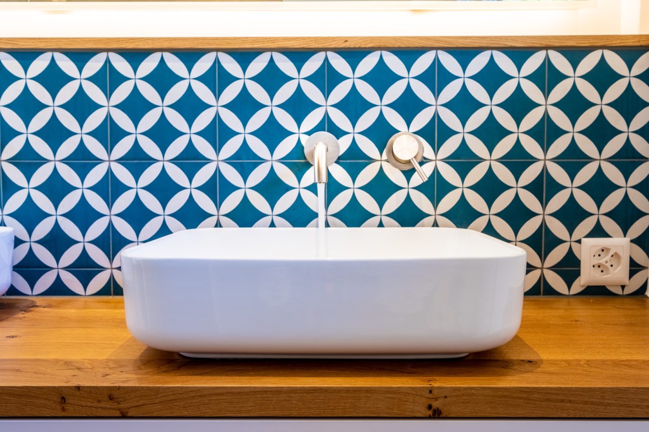 Bathroom backsplash with blue and white cement tiles, wooden counter and white sink