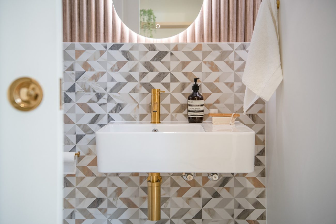 Bathroom with geometric peel-and-stick wall tile, wall-mounted sink and gold faucet