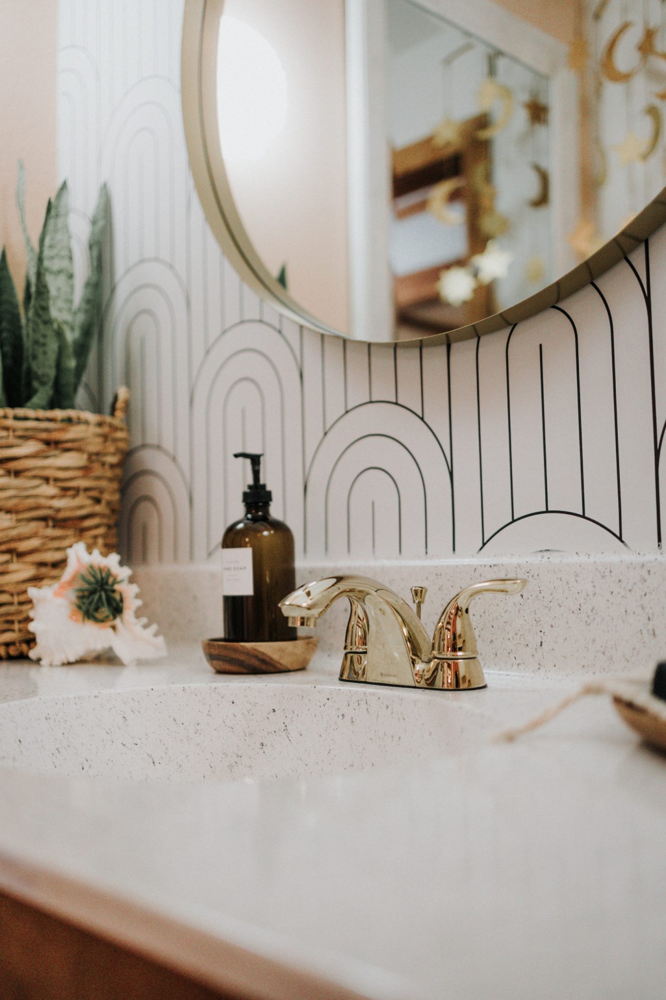 Bathroom with geometric wallpaper, quartz countertop and round mirror