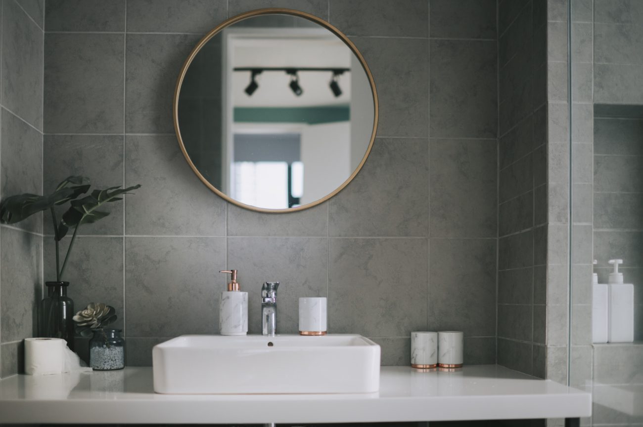 Bathroom with grey quarry tiles a rounded mirror and white sink
