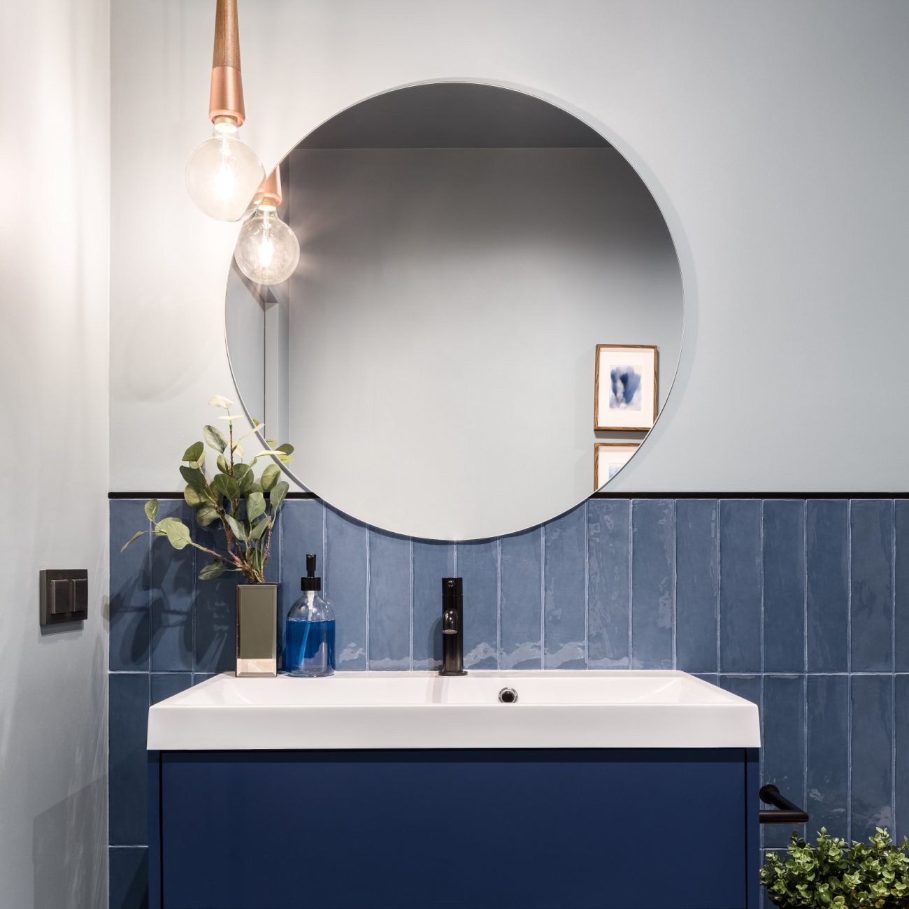 Designed bathroom with blue wall tiles with rounded mirror and blue and white vanity