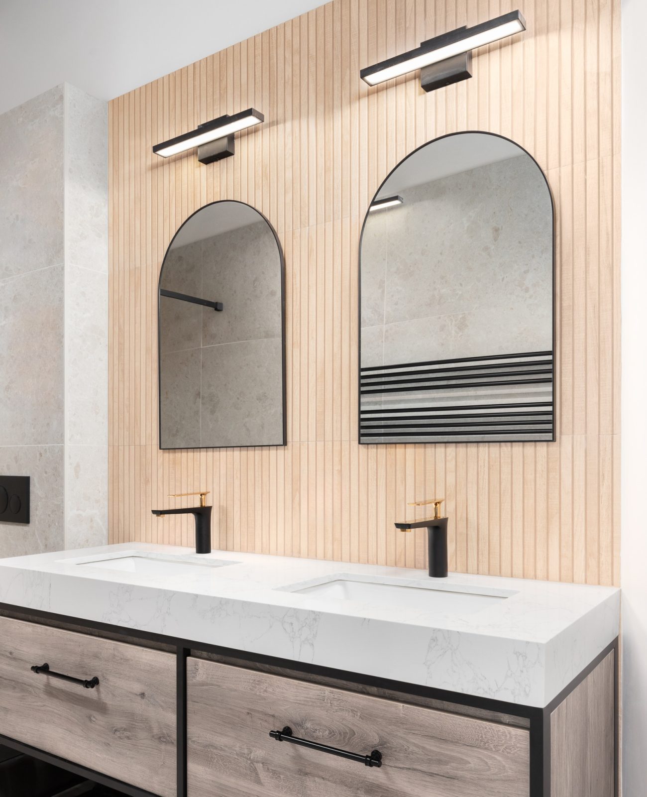 Modern bathroom with double vanity, white oak wood slat paneling on the wall and black arched mirrors