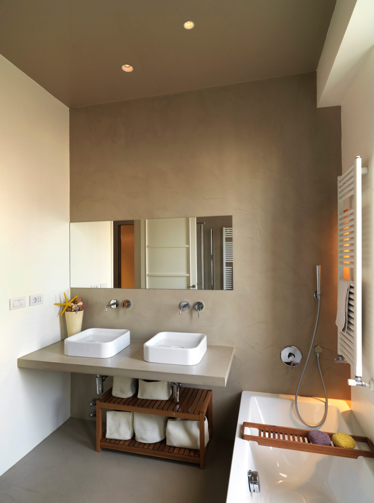 Modern interior bathroom with grey resin backsplash, two white vessel sinks and bath