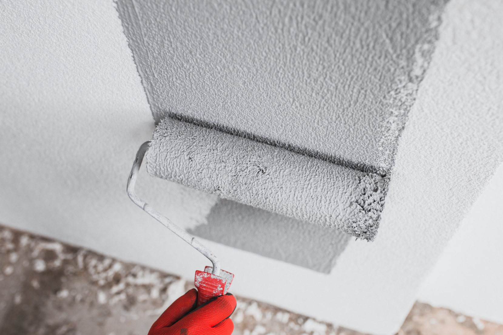 A contractor applies grey paint to an interior wall as part of building a house.