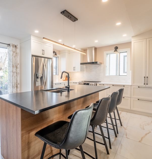 Modern white kitchen with white Shaker-style cabinets, quartz countertops, white ceramic backsplash, large island, white ceramic floor, and stainless steel appliances